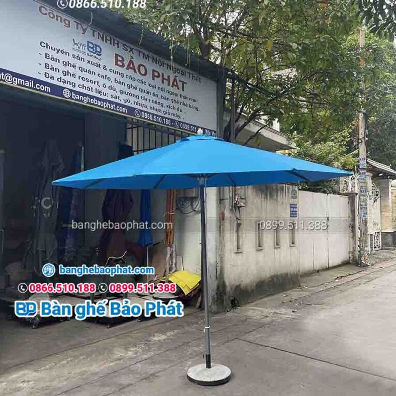 Mẫu dù che sân vườn màu xanh được làm từ vải cao cấp, khung dù bằng sắt bền bỉ, và đế dù được làm từ bê tông kết hợp với viền thép chắc chắn